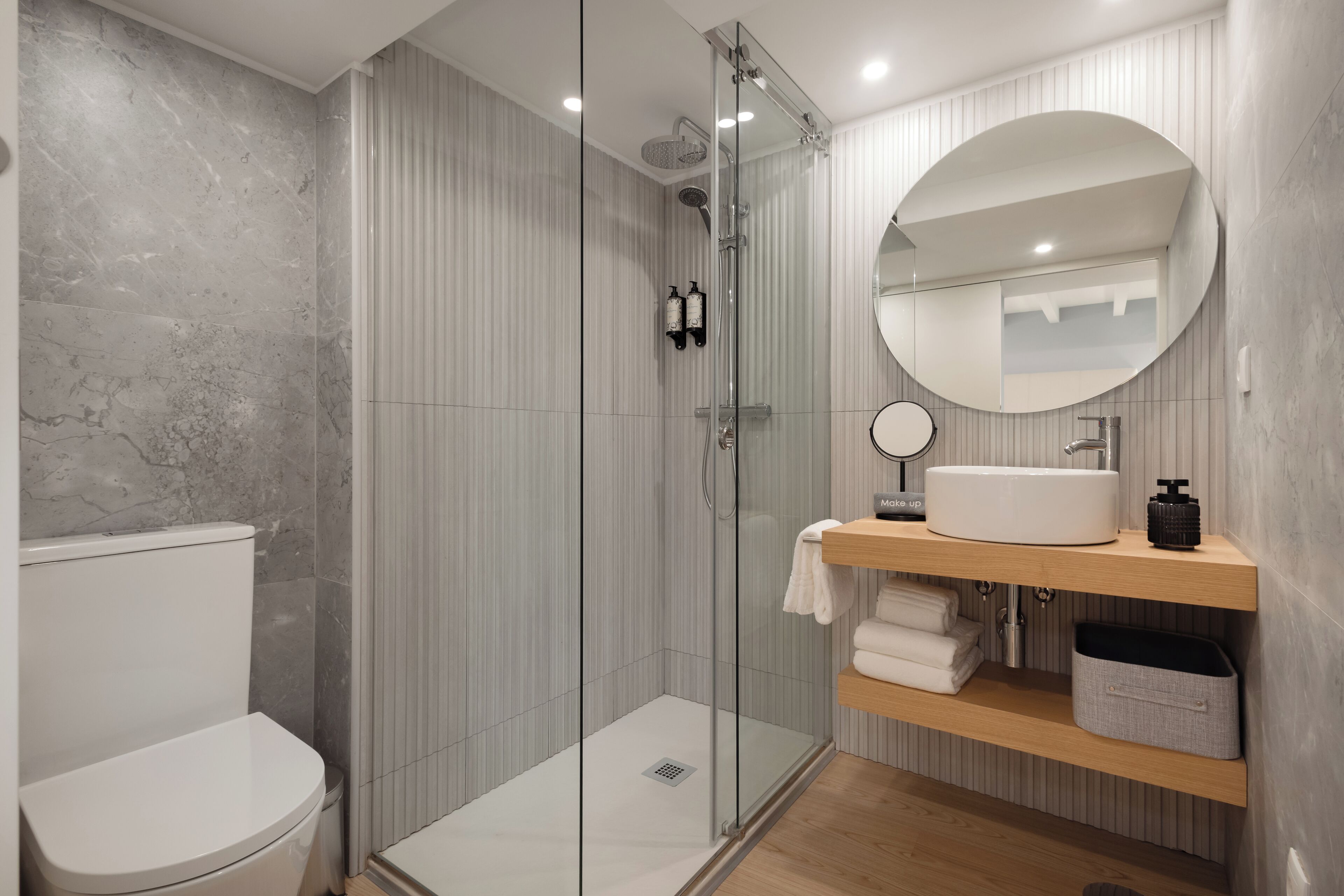 A modern bathroom with a glass-enclosed shower, a white toilet, a wooden vanity with a sink, and a mirror.
