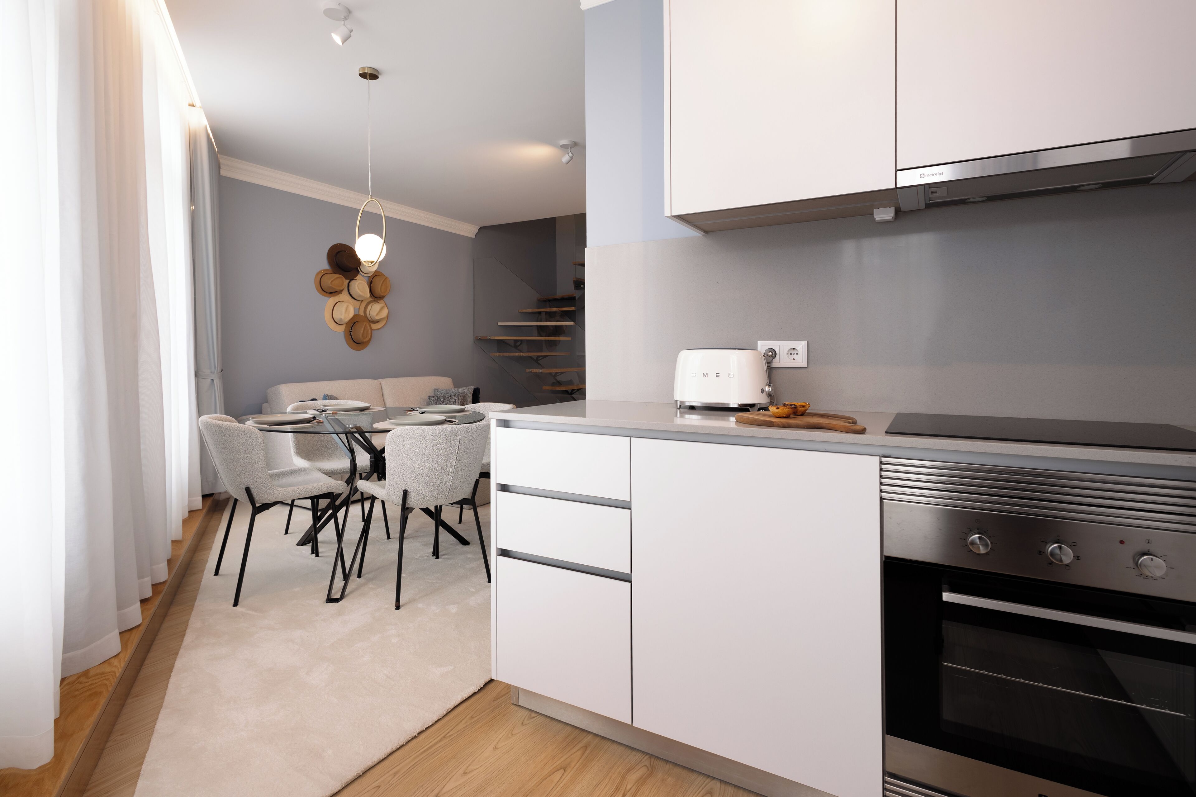 A modern kitchen with white cabinets, a built-in oven, and a dining area with a table and chairs.