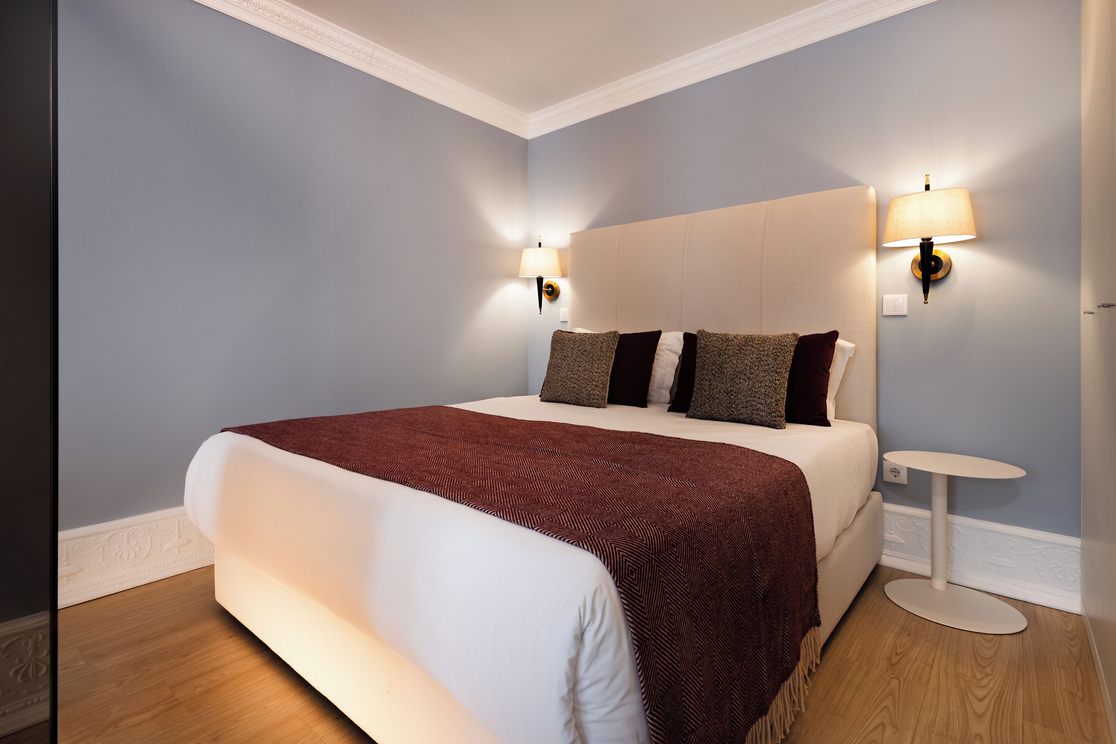 A bedroom with a large bed, two wall-mounted lamps, and a small round table.
