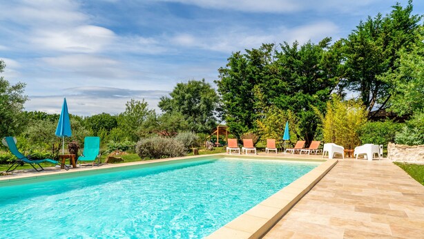 Une piscine entourée d’arbres et de verdure, avec des chaises longues et des parasols.