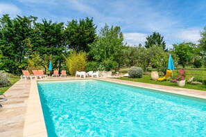 Ein Pool mit Liegestühlen und Sonnenschirmen, umgeben von viel Grün.