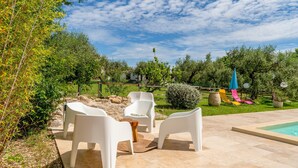 Une terrasse avec des chaises en plastique blanches, une petite table en bois et une piscine.