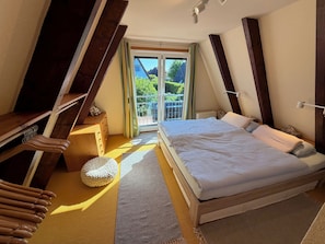 Une chambre à coucher avec un grand lit, une commode en bois, une petite table et une fenêtre donnant sur un paysage verdoyant.