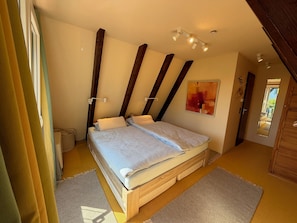 Une chambre à coucher avec un lit, des poutres en bois, un luminaire au plafond, un miroir et une porte.