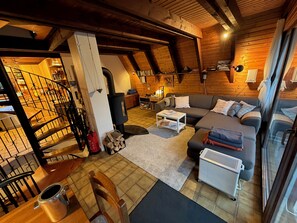 L’intérieur d’un chalet confortable, avec des murs en bois, comprenant un escalier, une cheminée, un canapé et un coin repas.