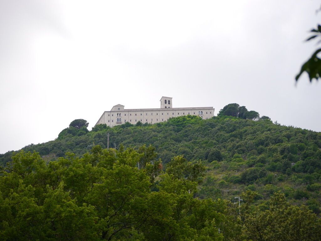 Un grand bâtiment rectangulaire, doté d’une tour centrale, entouré d’une végétation luxuriante et verdoyante sur une colline.