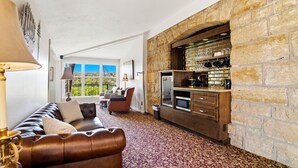 A living room with a leather sofa, a patterned carpet, a stone fireplace, and a view of greenery outside. - St. Croix Valley Inn (Shafer)