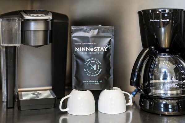 A coffee maker, a coffee pod, and two white cups on a countertop. - St. Croix Valley Inn (Shafer)