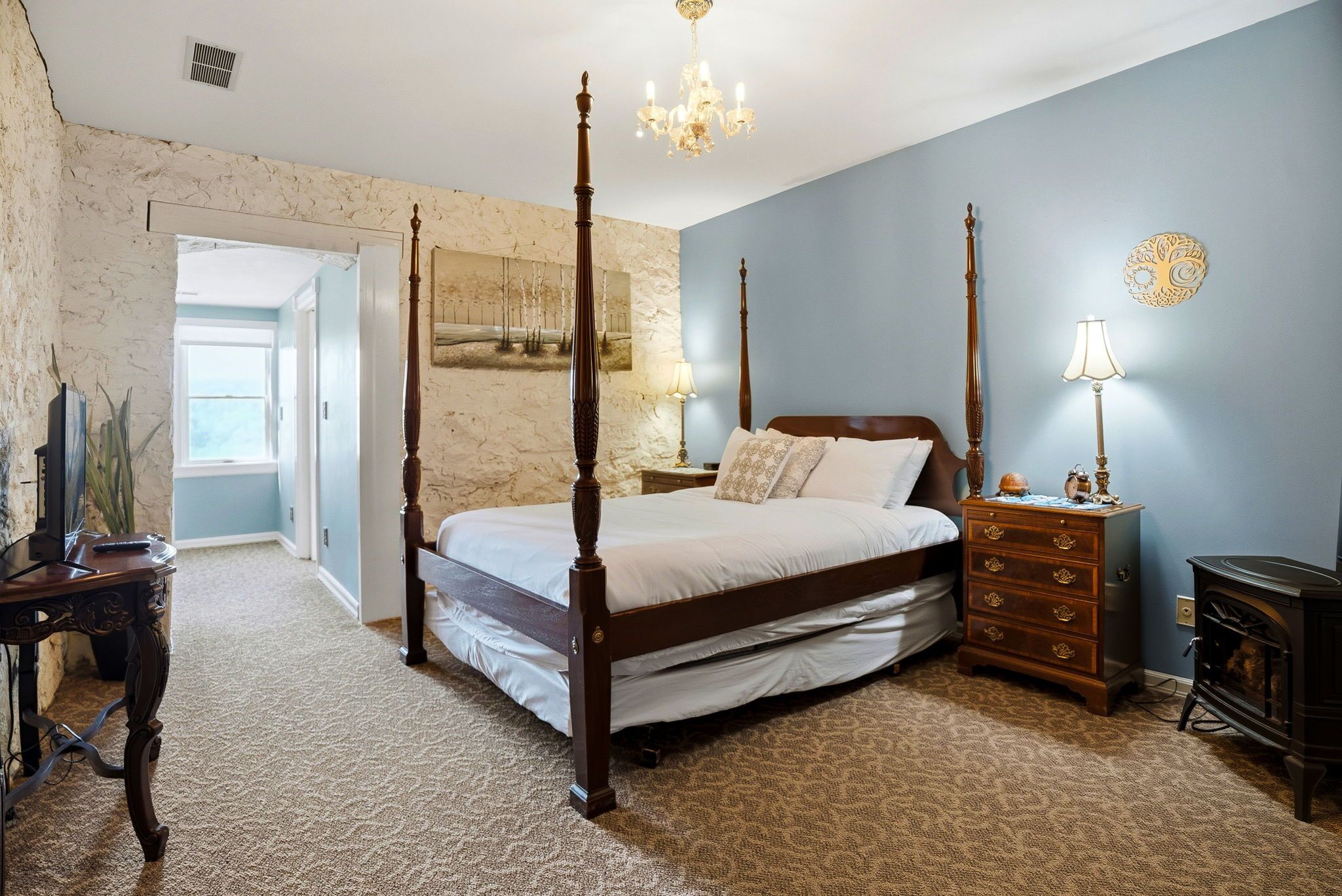 A bedroom with a four-poster bed, a dresser, a nightstand, a lamp, and a wall-mounted clock.