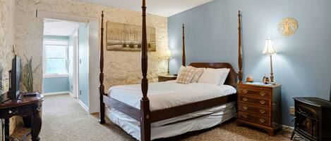 A bedroom with a four-poster bed, a dresser, a nightstand, a lamp, and a wall-mounted clock.