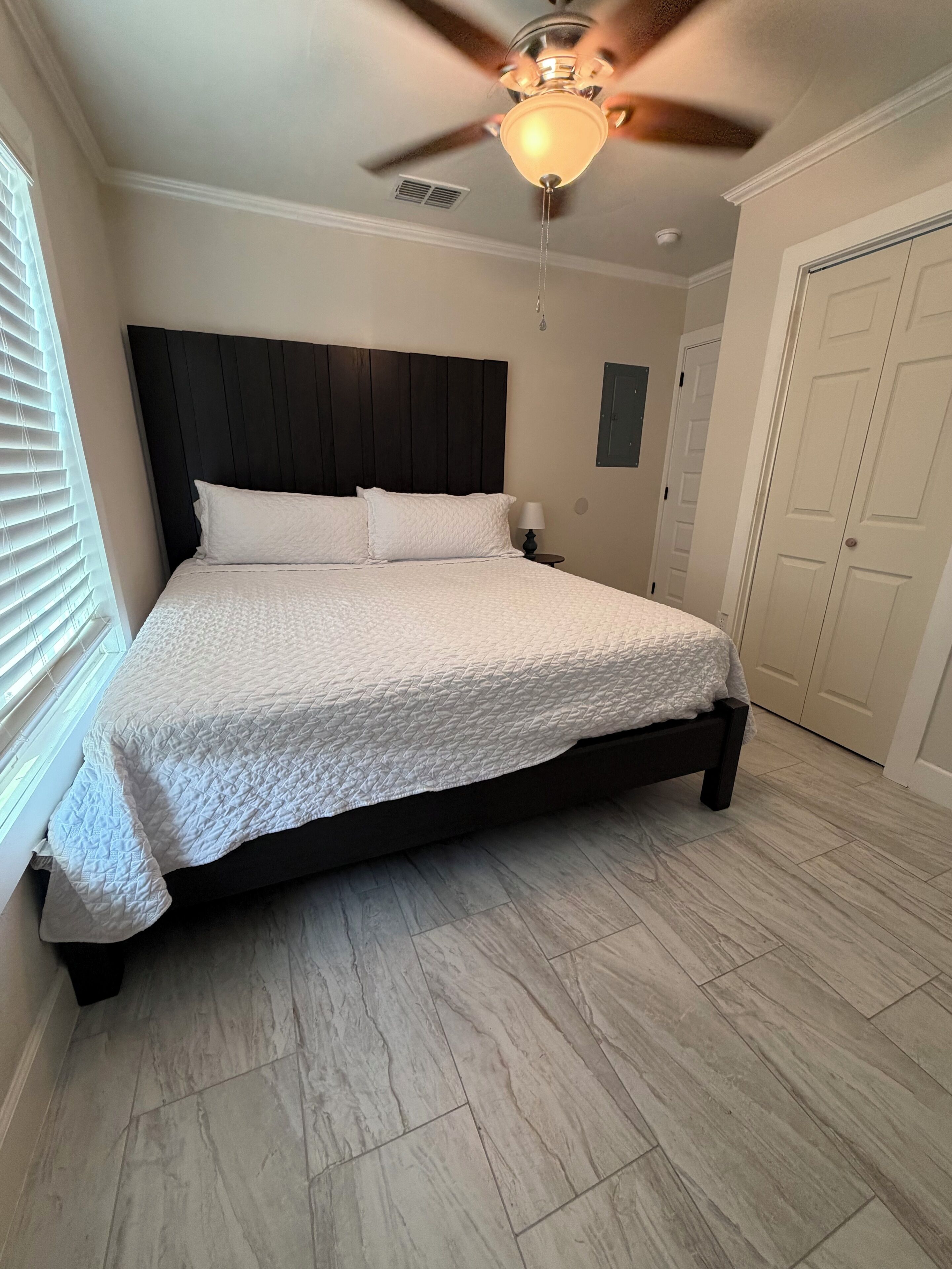 Une chambre à coucher avec un lit, un ventilateur de plafond, une table de chevet et une porte.