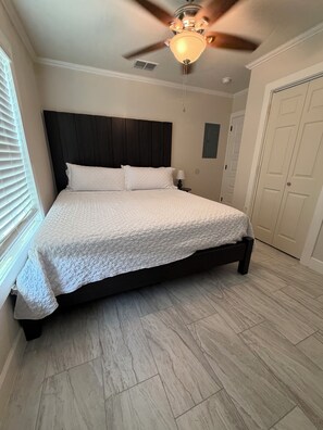 A bedroom with a bed, a ceiling fan, a nightstand, and a door.