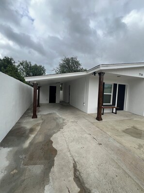 Un espacio al aire libre techado con suelo de concreto, columnas de madera y un banco.