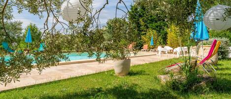 Un área junto a la piscina con césped, sillas de descanso y sombrillas.