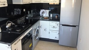 A compact kitchen with a black countertop, a built-in stove, a washing machine, and a stainless steel refrigerator. - Magnificent sea-view and waterfront apartment at Tamaris Dar Bouazzza (Tamaris)