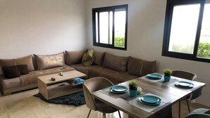 A modern living room with a wooden dining table set for four, a brown leather sofa, and a coffee table. - Magnificent sea-view and waterfront apartment at Tamaris Dar Bouazzza (Tamaris)