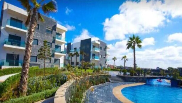 A modern hotel with a swimming pool, palm trees, and a clear blue sky. - Magnificent sea-view and waterfront apartment at Tamaris Dar Bouazzza (Tamaris)
