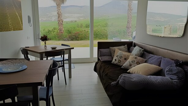 A room with a dining table, chairs, a sofa, and a large window with a view of a landscape. - Villa Degli Alberi with Garden, Private Terrace, Wi-Fi and Air Conditioning (Buseto Palizzolo)