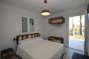 Ein Schlafzimmer mit Bett, Nachttisch, Kleiderschrank, Fenster und einer Tür zu einem Außenbereich.