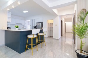 Une cuisine moderne avec des meubles blancs, un îlot central doté de tabourets et un grand réfrigérateur.