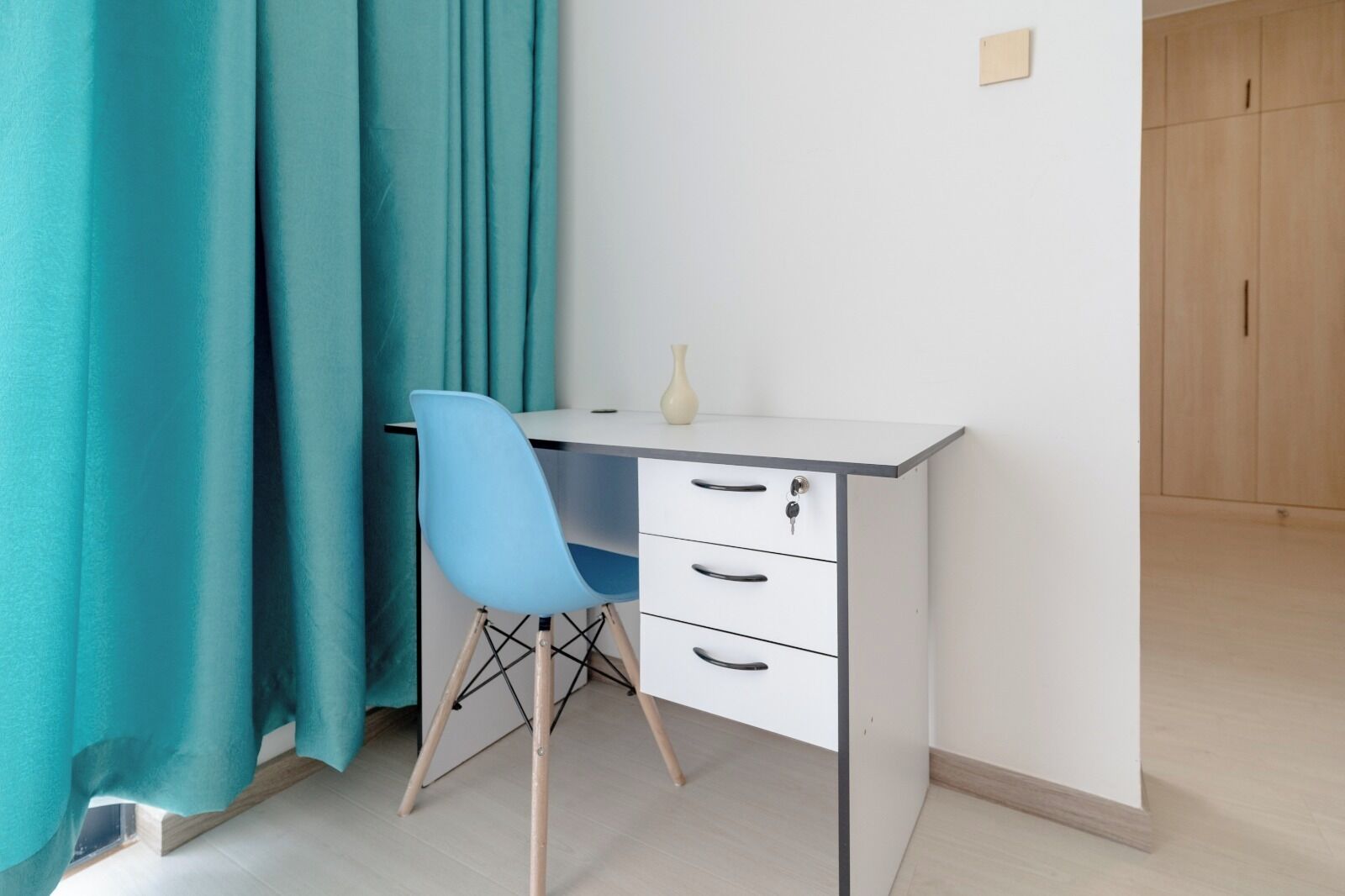 A small, modern room with a desk, chair, and a wardrobe.