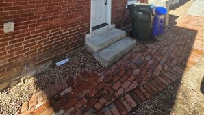A two-story brick building with a white door and windows. There are two trash bins outside. - Boutique Italian Village | OSU | 4BR | + 2 parking (Columbus)