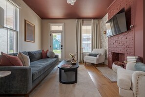 A living room with a grey sofa, a white armchair, a black coffee table, and a brick fireplace. - Boutique Italian Village OSU 4BR + 4 parking spots (Columbus)