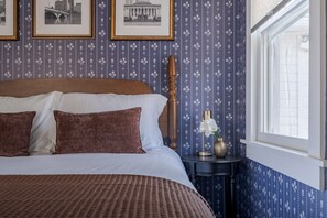 Ein Schlafzimmer mit einem großen Bett, einem Nachttisch mit einer Vase und einem Fenster mit Blick.