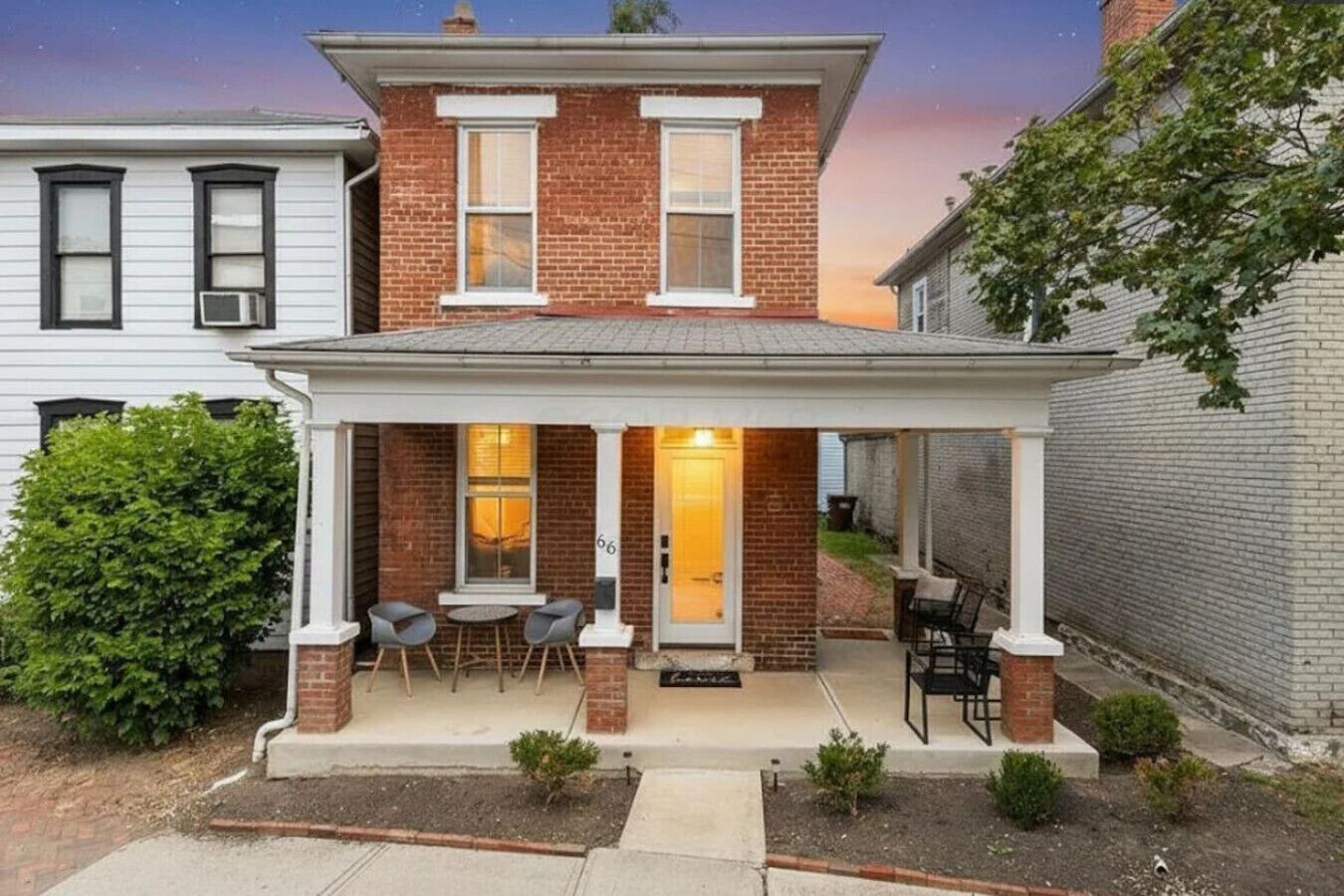 Une maison à deux étages, construite en briques, dotée d’un patio couvert et d’une porte d’entrée.
