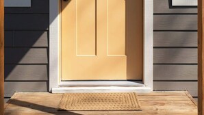 Une porte d’entrée avec une boîte aux lettres, un paillasson et une petite fenêtre au-dessus de la porte.
