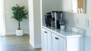 Une cuisine moderne avec des meubles blancs, un plan de travail en marbre, une machine à café et une plante en pot.