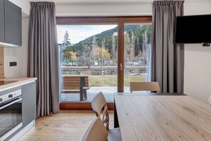 Una cocina moderna con horno empotrado, una zona de comedor con mesa y sillas de madera, y un ventanal con cortinas.