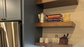 Una cocina con un refrigerador de acero inoxidable, una cafetera, un molinillo y un tarro de nueces sobre la encimera.