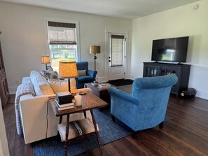 Una sala de estar con sofá, sillón, mesa de centro, lámpara, televisor y un mueble.