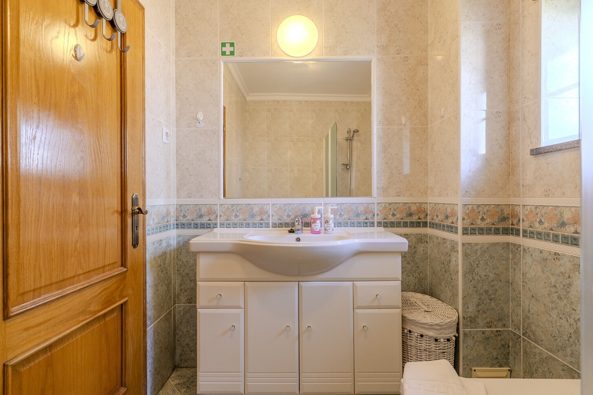 A bathroom with a wooden door, a white sink with a mirror above it, and tiled walls.