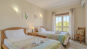 Een hotelkamer met twee bedden, een raam met gordijnen, een stoel en een wandairconditioner.