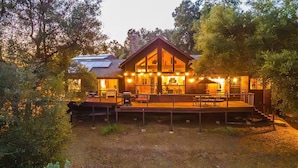 Een ruime, houten chalet met twee verdiepingen en een terras, omringd door bomen.