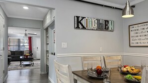 A dining area with a wooden table set for four, a kitchen sign above, and a welcoming message on the wall. - Walk to Downtown, Hot Tub, Game Room, Boat Parking (Branson)