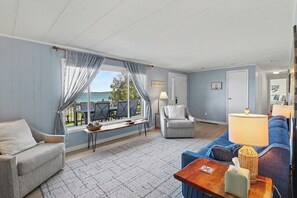 Una sala de estar con vista a un lago, un sofá, un sillón, una mesa y una lámpara.