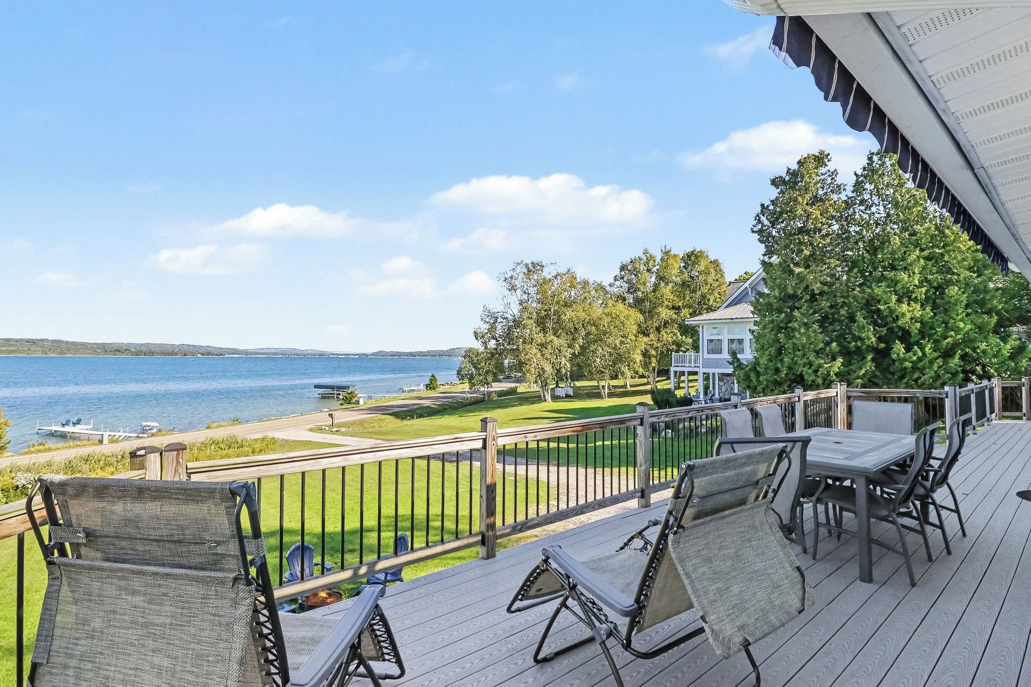 A deck with outdoor furniture overlooking a body of water and a grassy area.