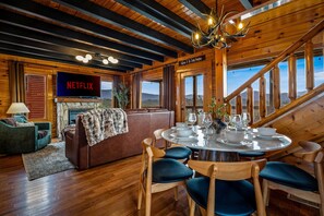 L’intérieur d’un chalet accueillant, avec une cheminée, une table à manger dressée pour quatre personnes et un grand écran de télévision affichant le logo « NETFLIX ».