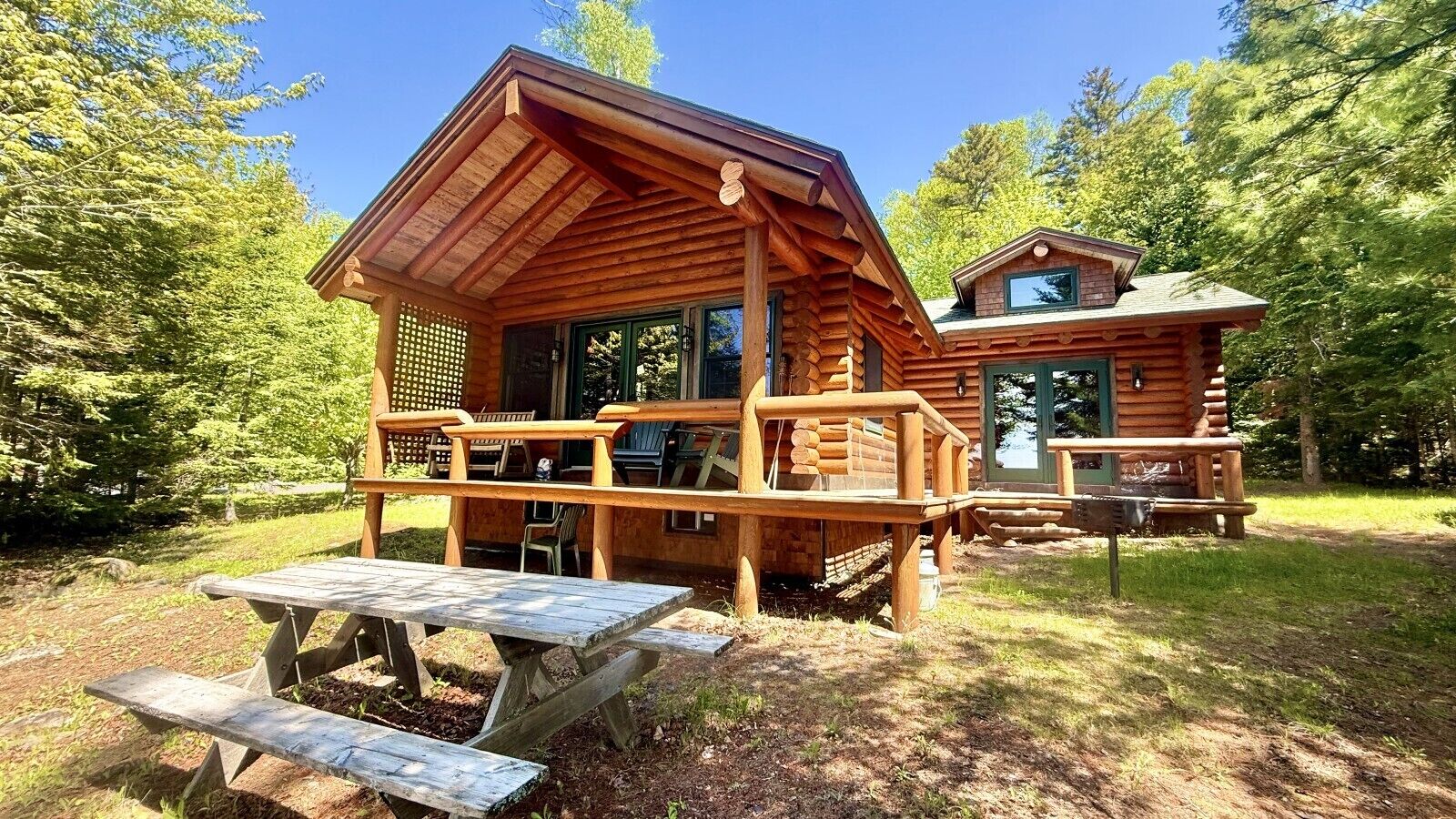 A rustic log cabin with a porch and picnic tables, surrounded by trees.