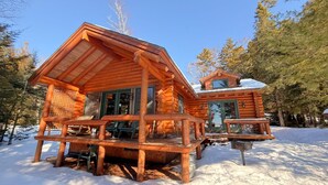 Une cabane en rondins dotée d’un porche et d’une autre cabane attenante.