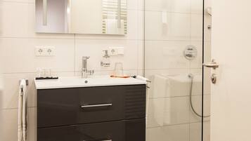 Un baño con un lavamanos blanco, un espejo, toallero y cabina de ducha de vidrio.