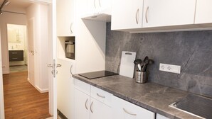 A modern kitchen with white cabinets, a granite countertop, and a built-in oven. - Hotel & Restaurant Wefers (Emsdetten)