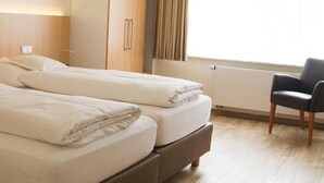 A hotel room with two beds, a chair, and a window with curtains. - Hotel & Restaurant Wefers (Emsdetten)