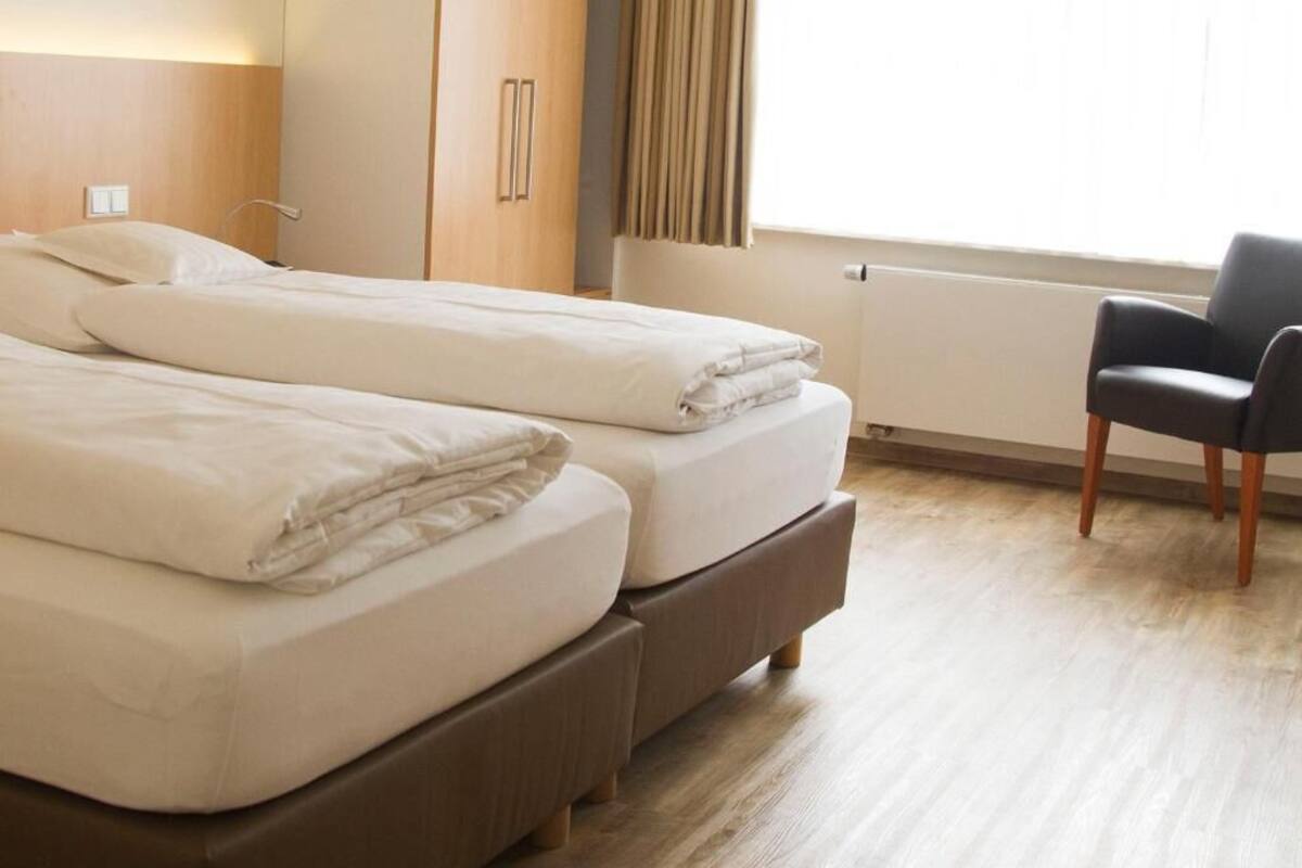 A hotel room with two beds, a chair, and a window with curtains.