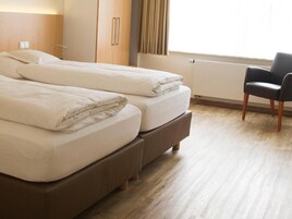 Habitación de hotel con dos camas, una silla y un ventanal con cortinas.