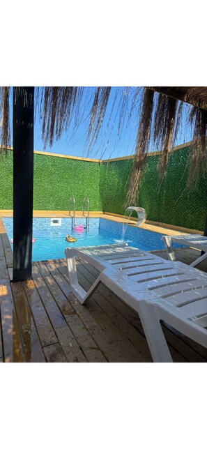 Une piscine avec une terrasse en bois, des chaises longues et un mur végétal.