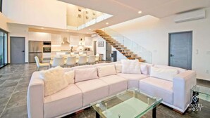 Ein modernes Wohnzimmer mit einem großen Ecksofa, einem Glastisch und einer Treppe zu einer oberen Ebene.